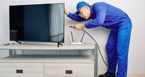 Serious young Vietnamese repairman installing tv set in apartment of customer